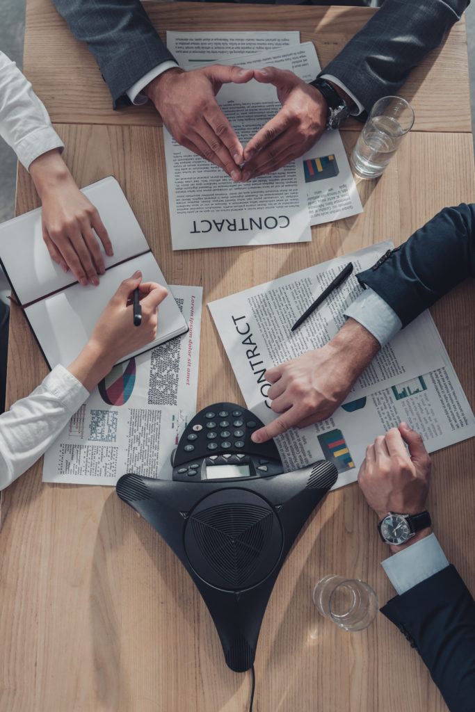 cropped shot of business people working with documents and speakerphone on table at modern office